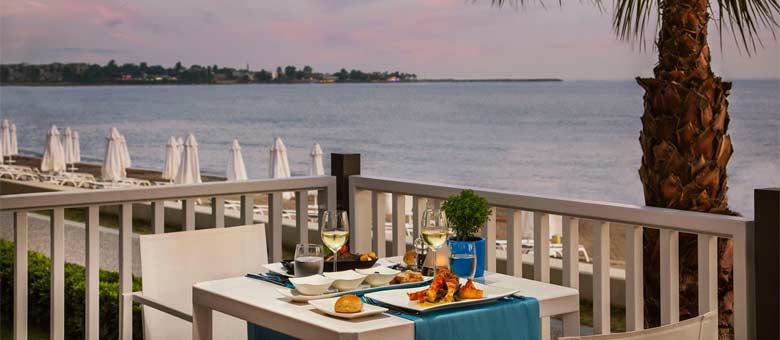 Overlooking the beach and sea, a table is set with delicious looking food and wine, ready for guests to enjoy their evening meal as one of the many restaurants available.
