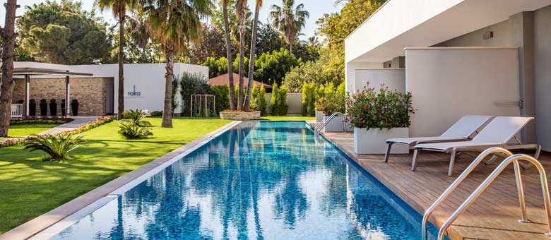 The lush green landscaped gardens of the hotel with a swimming pool adjacent to some swim-up rooms that provide guests direct access to a swimming pool from their accommodation, an example of the varied hotel facilities on offer at Acanthus Cennet Barut Collection