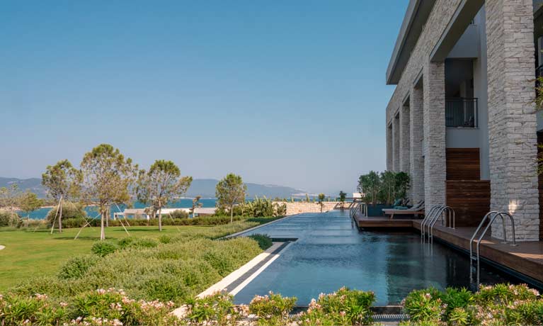 The landscaped grounds of the hotel on a deep blue day open out from a row of swim up rooms with the sea and beach in the background