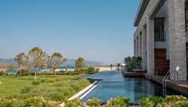 The landscaped grounds of the hotel on a deep blue day open out from a row of swim up rooms with the sea and beach in the background