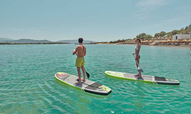 A couple using paddle boards supplied by the hotel, the sea is calm and the water clear on a bright sunny day