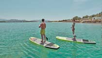 A couple using paddle boards supplied by the hotel, the sea is calm and the water clear on a bright sunny day