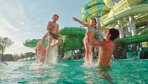 The large, fun slides of the water park can be seen behind a family having fun, playing in the swimming pool