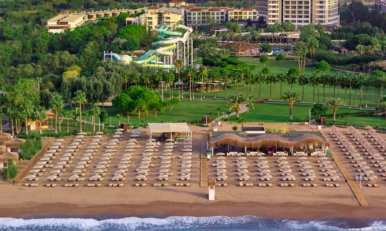 An aerial from the sea looking inland over a Barut Collection hotel, the sandy beach features sun loungers and umbrellas for guests to relax on their holiday
