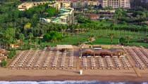 An aerial from the sea looking inland over a Barut Collection hotel, the sandy beach features sun loungers and umbrellas for guests to relax on their holiday