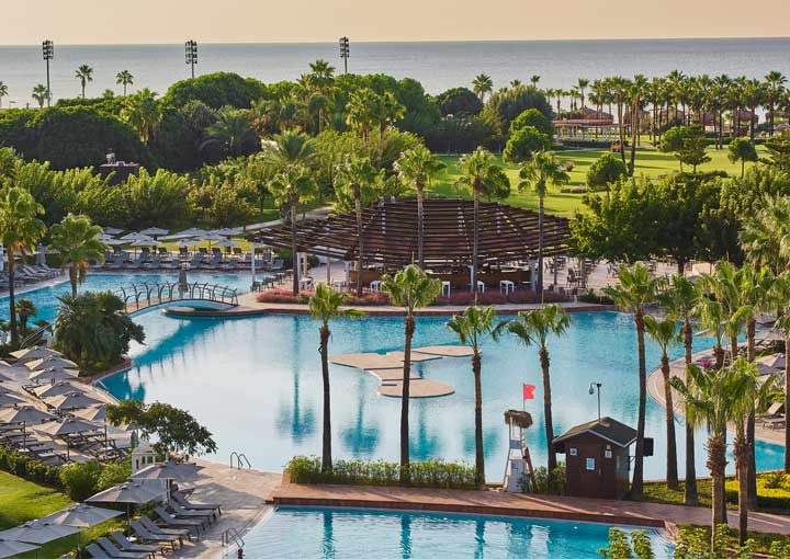 A view of the lush green gardens at Lara Barut Collection, in the foreground the hotel's main swimming can be seen surrounded by sun loungers and umbrellas ready for guests