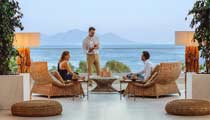 A couple relax at the Lobby Bar in front of beautful sea views while being served by a smiling waiter.