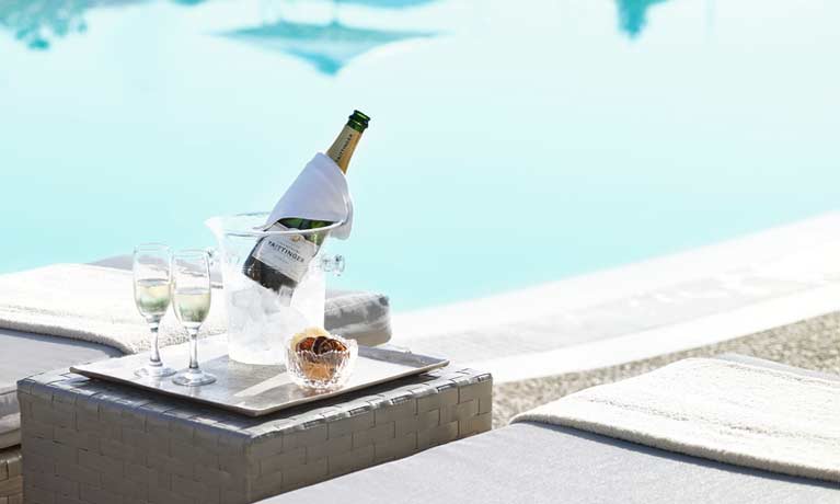A bottle of Tattinger Champagne chills in an ice bucket next to an inviting looking swimming pool.