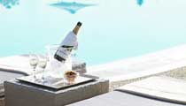 A bottle of Tattinger Champagne chills in an ice bucket next to an inviting looking swimming pool.