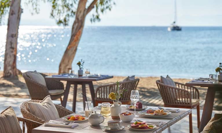 Al fresco dining at an Ikos Resort, a table is set for dinner on a terrace overlooking the sea on a sunny clear day.