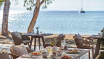 Al fresco dining at an Ikos Resort, a table is set for dinner on a terrace overlooking the sea on a sunny clear day.
