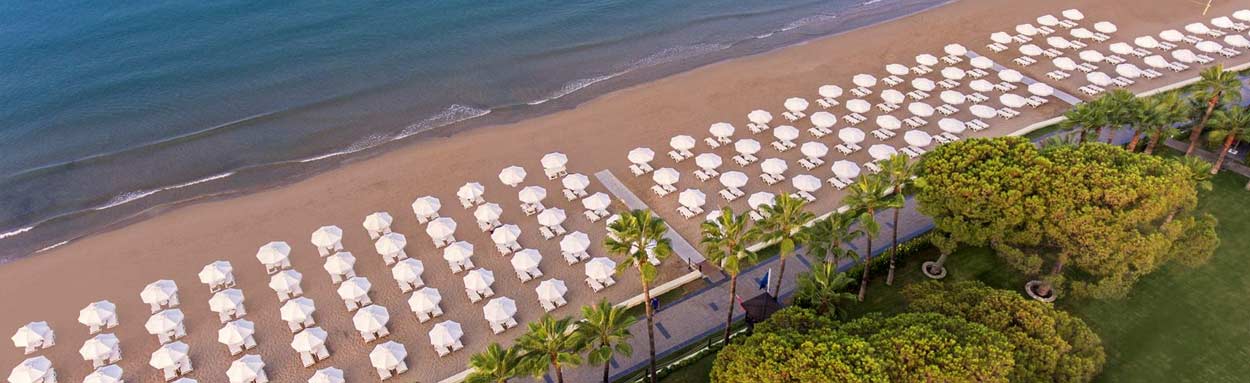 An aerial view of the beach outside Acanthus Cennet Barut Collection, the green landscaped gardens give way to a soft sandy beach with plenty of sun loungers and shade umbrellas for guets use.