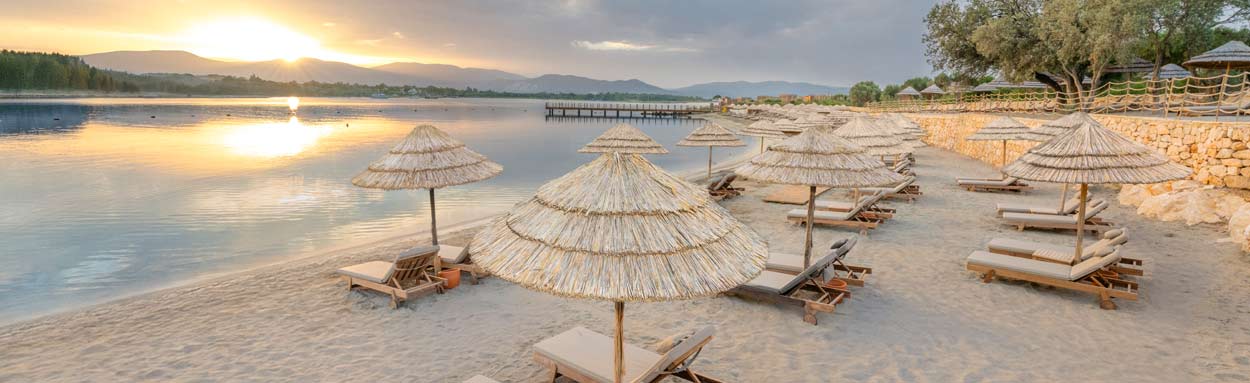 A panoramic view of the beach at sunset with sun loungers and umbrellas set out for guests convenience at  Anda Barut Collection
