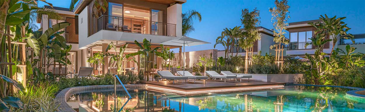 Outside the villa at sunset looking over the still waters of the swimming pool towards the villa which is illuminated and welcoming